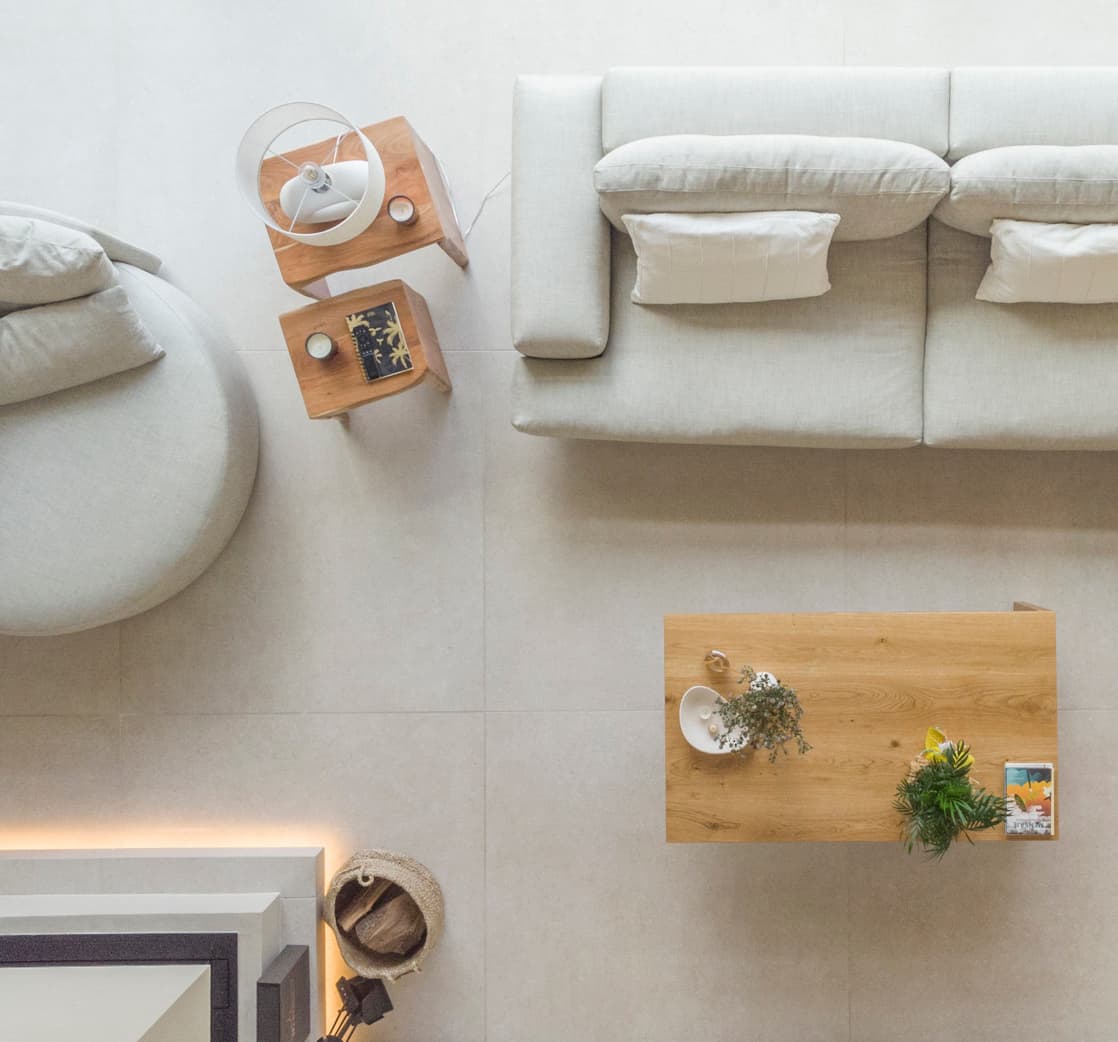 Top view of a minimalist living room with a beige sofa, round chair, wooden coffee table with plants, and a small side table with a lamp.