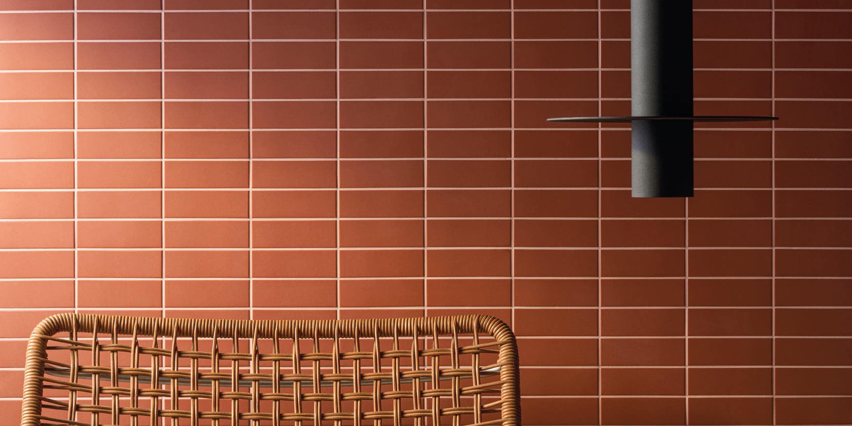 Woven chair against a wall of horizontal, rectangular, reddish-brown tiles using Fugabella