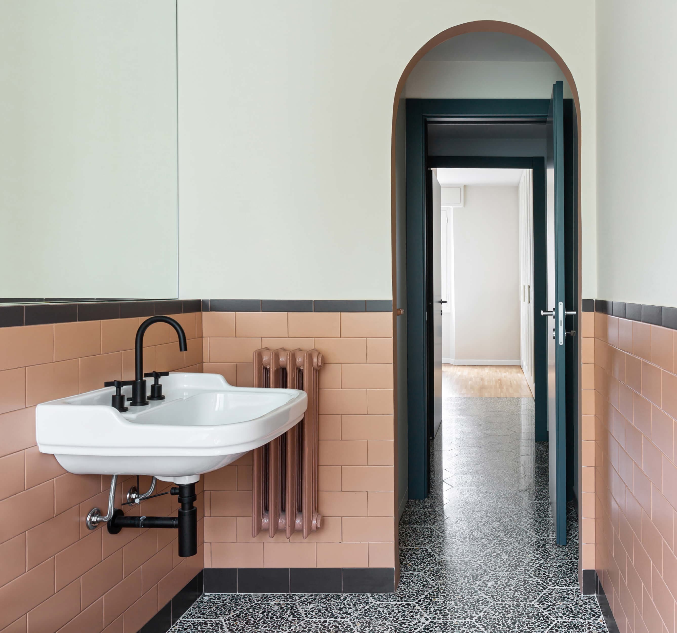 Bathroom with a white sink, black faucet, and peach tiles. An open door leads to a hallway with patterned flooring and white walls.