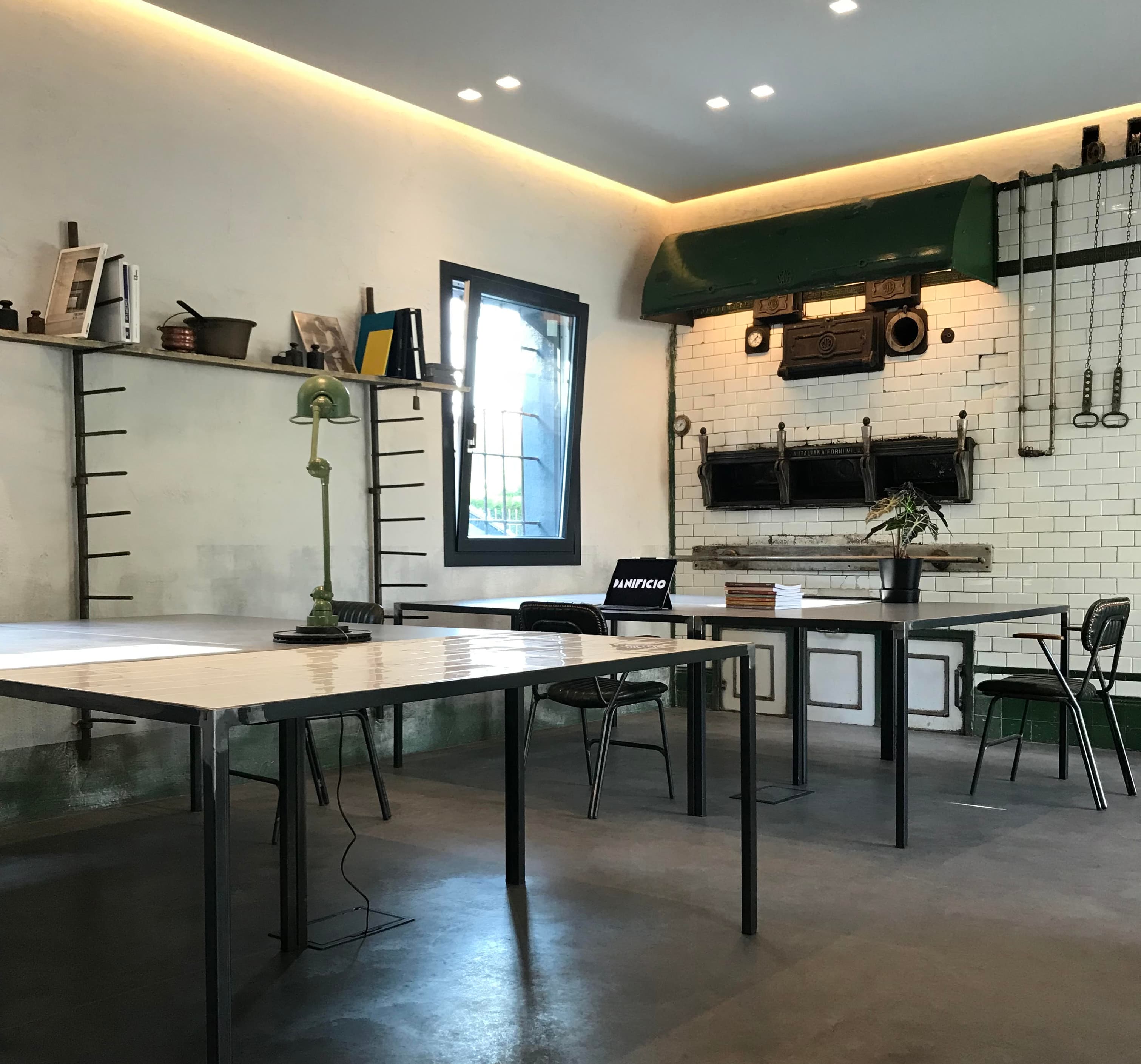 Industrial-style room with metal tables, chairs, and wall shelves. White tiled wall features vintage tools and decor.