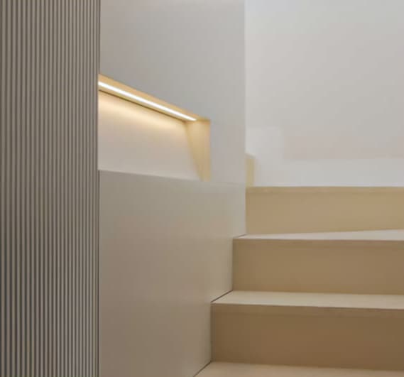 Minimalist staircase with beige steps, a ribbed wall, and soft recessed lighting on the left, creating a serene, modern atmosphere.