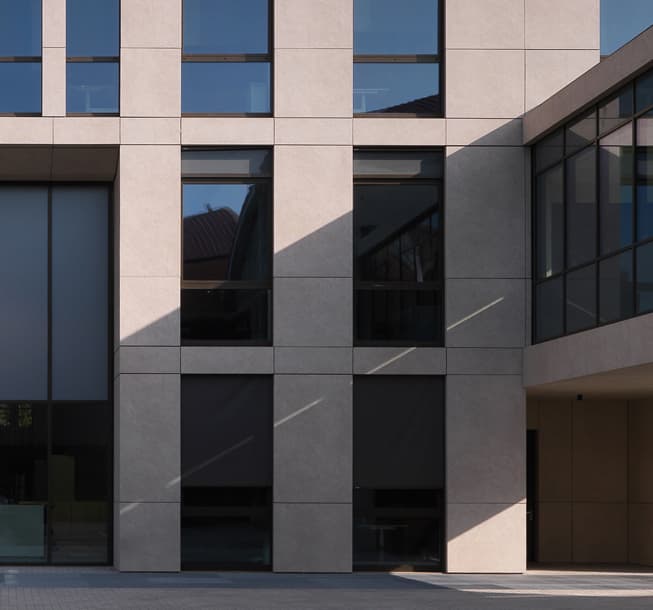 Modern building facade with large windows and geometric patterns, casting sharp shadows on the ground.