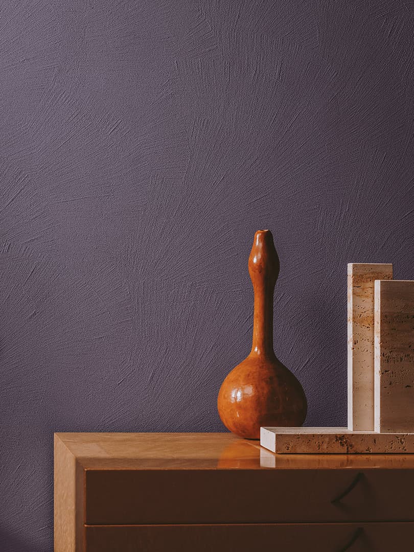 A wooden vase and stone slabs on a wooden cabinet against a textured purple wall.